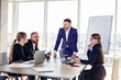 © DSMT - Confident businessman makes a presentation of a new project in the boardroom at a company meeting. Beautiful auditors talk with different partners about the business using a whiteboard and graphs.
