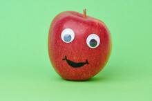 Red Apple With A Funny Lauging Face On Green Background