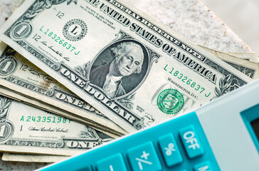 One dollar bills next to a blue calculator. Concept of little money to pay as debts. Finance and economy.
