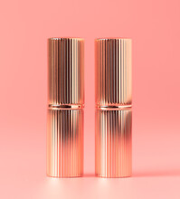 Two Lipsticks In Gold Rippled Packaging On A Pink Background.