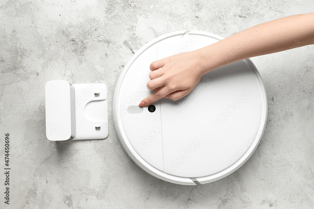 Female hand with modern robot vacuum cleaner on grunge background