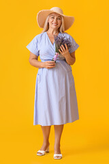 Poster - Elegant mature woman in straw hat holding bouquet of beautiful flowers on yellow background