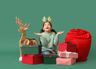 Poster - Funny little girl with wooden reindeer and Christmas gifts on color background