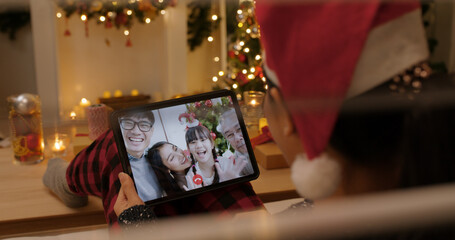 X'mas asia happy woman relax smile laugh greet in digital tablet screen remote talk to child kid friend at night online video VoIP party sit on cozy sofa at home enjoy good warm time winter season.