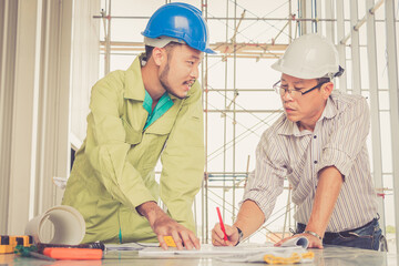 Engineer and worker looking home plans with helmet, craftsman tool and home model on workplace at construction site.