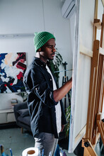Focused Peaceful Black Man Painting On An Easel Inside Of His Apartment
