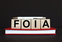 FOIA. text on wooden cubes. On a black background. red notepad. pen