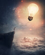 © psychoshadow - Creative idea concept with a person on the edge of a cliff holding the string of a lightbulb kite or a bulb balloon. Surreal adventure, conceptual scene, genius thinking