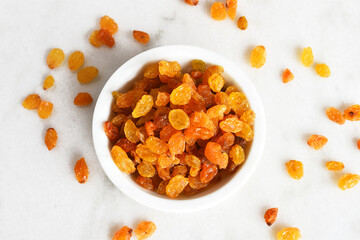 A top view image of fresh yellow seedless raisins in a white bowl on a marble table top. 