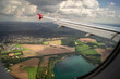 Ein Blick aus einem Fenster eines Flugzeugs mit Blick über einem See und Felder mit schönen dicken Woken am Himmel. 