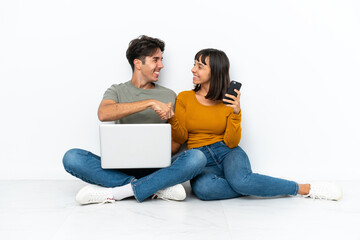 Wall Mural - Young couple with a laptop and mobile sitting on the floor handshaking after good deal