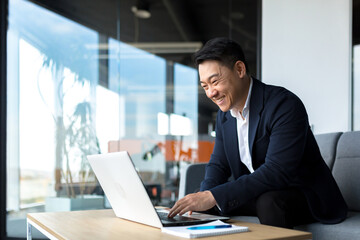 Senior Asian business man working on laptop online, smiling and rejoicing, happy boss business owner working in office