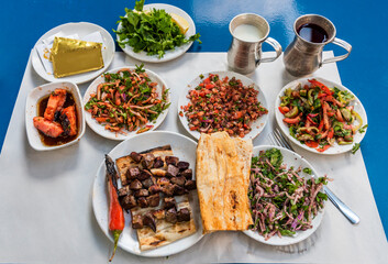 Ciger Sis Kebap in Adana, Turkey. Traditional Liver Shish Kebab in restaurant. Liver skewers presentation with different salads, ayran and turnip on table.