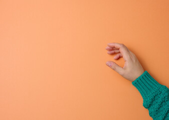 Wall Mural - female hand on an orange background, part of the body is holding the subject