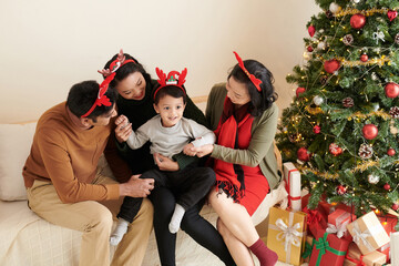 Wall Mural - Cheerful parents and grandmother playing with happy little kid when spending time at home on Christmas