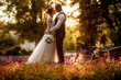 Bride and groom stand in a beautiful green garden on a warm autumn day. Newlyweds walk along the trees alley in the park. Wedding walk of the bride and groom at sunset. Beautiful kiss of newlyweds