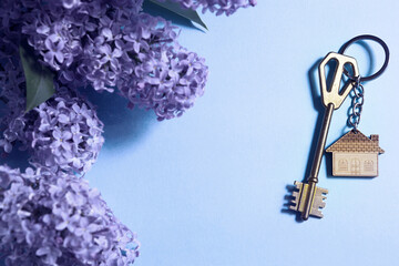 house key with keychain on blue spring background and lilac branches.summer holiday home, booking co