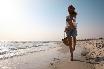 Wall Mural - Woman with beach bag walking on sunlit seashore