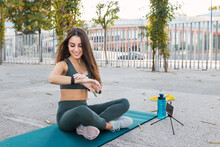 Smiling Athlete Watching Time On Exercise Mat In Public Park