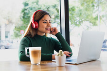 Smiling Businesswoman With Headphones And Mug Working On Laptop In Coffee Shop