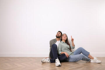 Wall Mural - Young couple sitting on floor near white wall indoors. Space for text