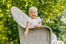 A Clumsy Baby Smeared With Chocolate. The Baby Is Enjoying Childhood, A Blue-eyed Child In A White Bodysuit Leaning Against The Side Of A Large Canvas Beige Chair. Enjoying The Playing In The Garden