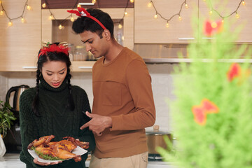 Wall Mural - Young couple discussing fried chicken they prepared for Christmas dinner