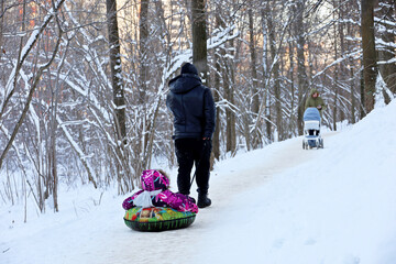 Family leisure in winter park, man rides the child on snow tube. Father with kid, sledding after snowfall