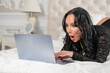 © Михаил Решетников - A sexy brunette with big breasts dressed in black underwear lies on the bed and flirts over video communication on a laptop. The woman works as a web model