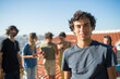 © KAMPUS - Portrait of man with curly hair at party. Young guy in black T-shirt looking at camera. Friends of different nationalities in background. Party, friendship concept