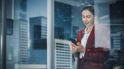 Aufkleber - Portrait of Stylish Businesswoman Using Smartphone, Looking out of Window on a City. successful Female CEO Working on Mobile Phone, Negotiating Purchase of Online Shopping e-Commerce Startup Software