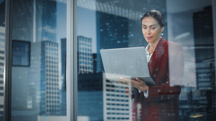 Poster - Portrait of Stylish Businesswoman Using Laptop, Looking out of Window on a City. successful Female CEO Working on Computer, Negotiating Purchase of Online Shopping e-Commerce Startup Software
