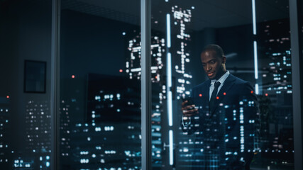 Successful Black Businessman in a Tailored Suit Standing in His Office Looking out of the Window on Night City. Successful Investment Manager Working Late. Stylish Outside Shot