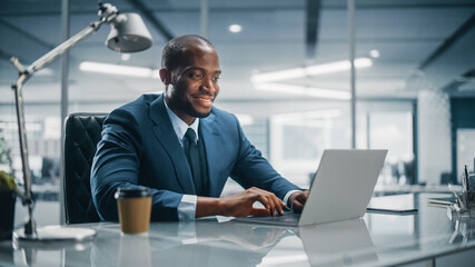 Top Management Modern Office: Successful Black Businessman in Tailored Suit Working on Laptop Computer. Professional African American CEO Managing Investment Strategy. Portrait of Top Manager