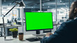 Successful Black Businessman Sitting at Desk Working on Green Screen Laptop Computer in Office. African American Businessperson using Chroma Key Display. Over the Shoulder Shot