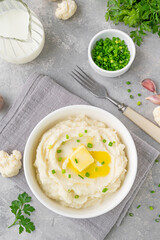 Wall Mural - Cauliflower puree with butter and green onions in a white bowl on a gray concrete background. Healthy food. Copy space.