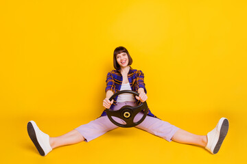 Sticker - Portrait of attractive cheerful girl sitting holding in hands steering wheel having fun isolated over bright yellow color background