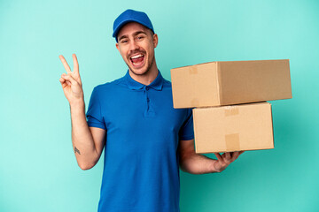 Wall Mural - Young delivery caucasian man isolated on blue background joyful and carefree showing a peace symbol with fingers.