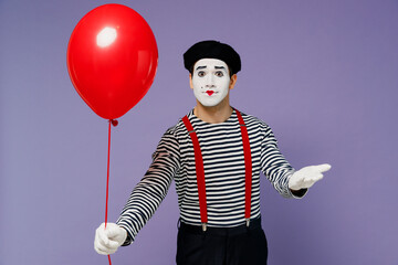 Wall Mural - Vivid happy young mime man with white face mask in striped shirt beret hold give present colorful air inflated helium balloon to you isolated on plain pastel light violet background studio portrait.