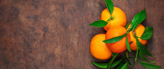 Wall Mural - Mandarines oranges fruits or tangerines with green leaves on a dark wooden table. Copyspace.