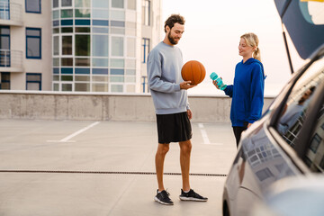 Wall Mural - Young man and woman smiling and talking during workout on parking