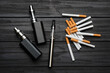 © New Africa - Cigarettes and different vaping devices on black wooden background, flat lay. Smoking alternative