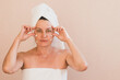 Middle-aged woman with a towel on her head, no makeup, applies cream to her face and makes massage. Facial skin care