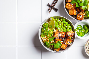 Wall Mural - Vegan noodles ramen soup with marinated tofu, edamame beans and hot peppers in gray bowls.