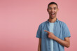 studio portrait of middle age middle eastern man wears blue shirt points aside with positive, happy facial expression isolated over pink background