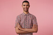 studio portrait of middle age middle eastern man wears checkered shirt keeps his hand crossed on chest with smile on his face. isolated over pink background