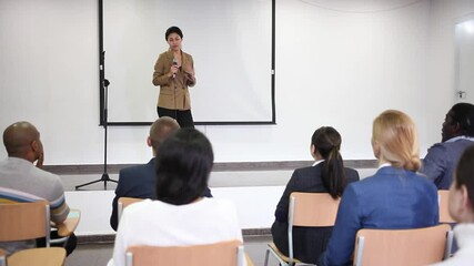 Wall Mural - Young woman motivational coach giving lecture at business convention at conference hall. High quality FullHD footage