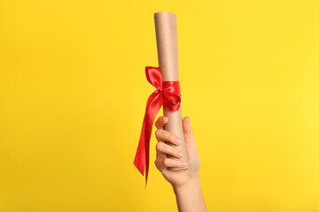 Wall Mural - Student holding rolled diploma with red ribbon on yellow background, closeup