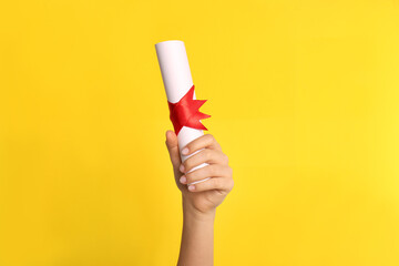 Wall Mural - Student holding rolled diploma with red ribbon on yellow background, closeup