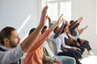 © Studio Romantic - Diverse mixed race male female audience raising hands. Active multiracial multiethnic men and women sitting in row with hands up to ask coach questions after interesting talk or engaging master class